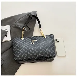 Detalle del bolso tote negro con estampado geométrico, colgante de ciervo dorado y cadena