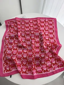 Detail of pink satin square scarf with red heart patterns on a white table