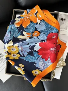 Détail d'un foulard en soie à fleurs avec bord orange dans un plateau en bois élégant