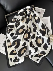 Detailed close-up of premium leopard print silk scarf with black borders on leather background