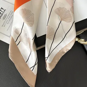 Detailaufnahme des Seidenschals mit eleganten Ginkgoblatt-Prints und schicken orangefarbenen Blöcken