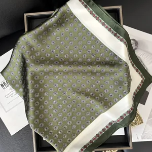 Pañuelo de seda verde oliva con diseño floral geométrico y borde crema en bandeja
