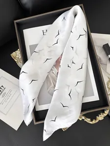 Detail of elegant white silk scarf with bird prints on a tray with lifestyle accessories