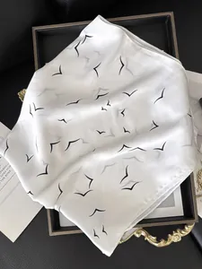 Close-up of white silk scarf with minimalist black bird print on elegant metal tray