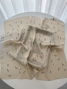 Detail of elegant beige silk square scarf with minimalist black bird print on white table