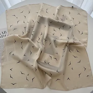 Close-up of lightweight champagne silk scarf featuring black flying bird print patterns
