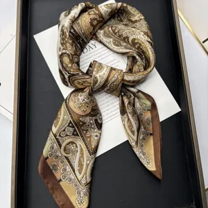 Elegant bohemian paisley silk scarf with gold and brown patterns on a black tray
