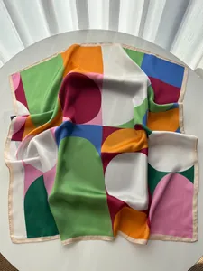 Detailed view of square silk scarf featuring modern colorful geometric patterns on white table