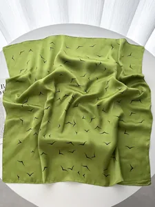 Close-up of grass green silk scarf featuring black abstract bird print and smooth texture