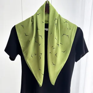 Detailed view of green square scarf with black abstract bird pattern on a black shirt
