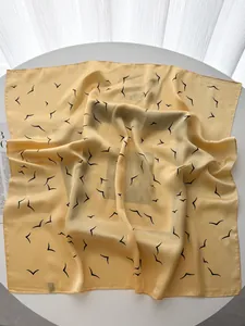 Detailed view of yellow silk scarf with black seagull print on white table
