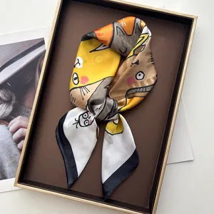 Détail d'un foulard en soie jaune avec imprimé chat et bordures noires sur un plateau