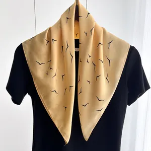 Detail view of smooth yellow silk scarf featuring an elegant black bird print pattern