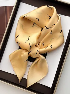 Close-up of a yellow satin square scarf featuring minimalist black bird patterns