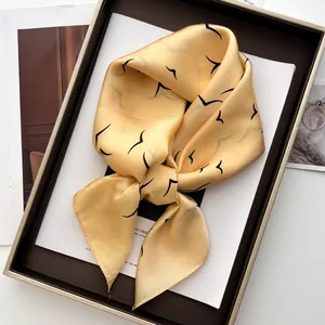 Detail view of yellow silk square scarf with black bird print tied in a decorative knot