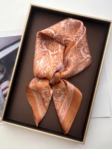 Detailed view of the vibrant orange and white silk scarf with abstract patterns in a box