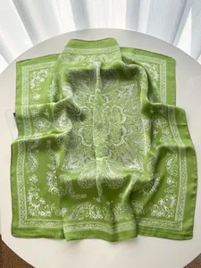 Detail of green paisley silk scarf with vintage floral print on a white surface