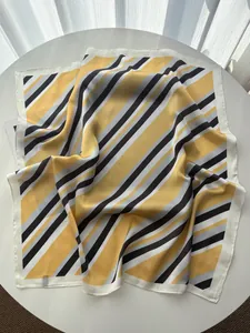 Close-up of vibrant yellow and black striped silk scarf with fine stitched edges on table