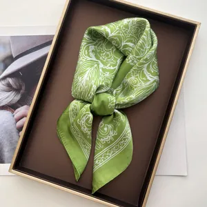 Detail of a bright green silk scarf with white floral patterns in a luxury gold-rimmed gift box