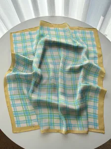 Detailed view of light blue and green plaid silk scarf with bright yellow border trim