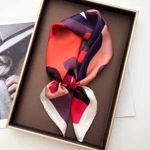 Silky square scarf with red geometric patterns placed on a premium metal display tray