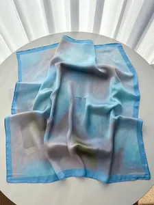 Gros plan d'un foulard en soie élégant avec bords bleu clair et imprimé abstrait sur table blanche