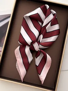 Close-up of a striped silk scarf tied in a bow inside a premium gold-trimmed display box