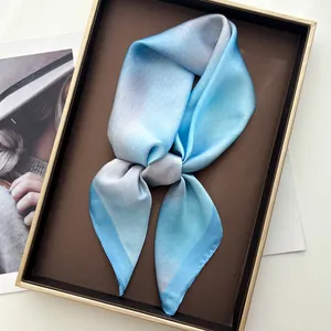 Gros plan détaillé d'un foulard en soie dégradé bleu présenté dans un coffret cadeau