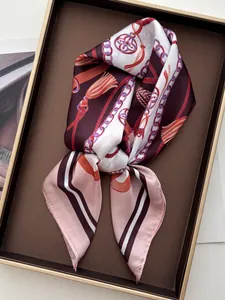 Detailed close-up of a silk scarf with classic chain and tassel print in a luxury gift box