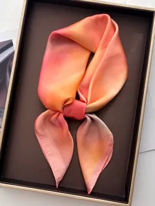 Détail macro d'un foulard élégant en soie dégradé rose et orange dans un coffret cadeau