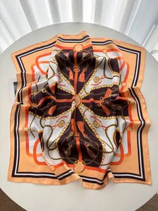 Detail of satin silk scarf featuring orange equestrian chain patterns and tassel prints