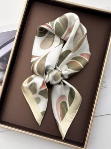 Detail of silk-like scarf with leaf prints folded in a brown tray with golden edges