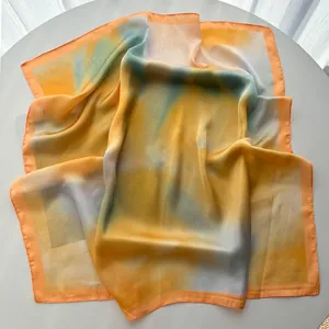 Détail d'un foulard carré en soie avec dégradé aquarelle dans les tons orange et bleu clair