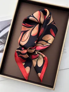 Detailed view of silk square scarf featuring orange leaf patterns and red hem on a display tray