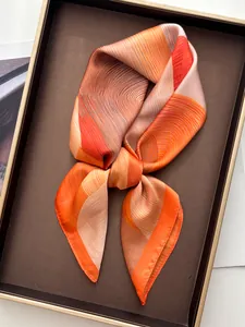 Close-up of silk square scarf with orange geometric patterns on a brown tray