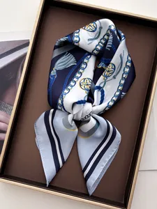 Close-up of silk scarf with navy chain and tassel print on a gold-rimmed tray