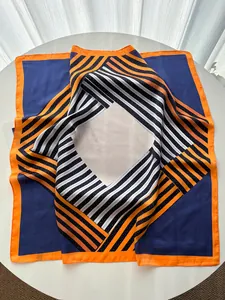 Détail du foulard en soie à rayures géométriques avec bordure orange sur table blanche