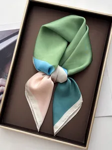 Detail of silk-like square scarf in green and blue color blocks in a golden gift box