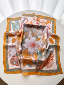 Dettaglio della sciarpa in seta con stampe di magnolia e bordo arancione su tavolo bianco