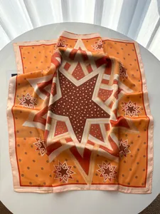 Detail eines orangefarbenen Seidentuchs mit Sterndruck und Satin-Textur auf weißem Tisch