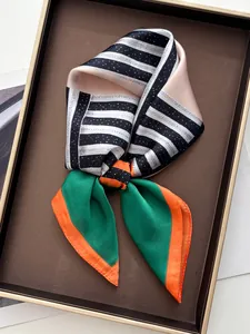 Détail d'un foulard en soie aux rayures géométriques avec un ourlet orange sur plateau