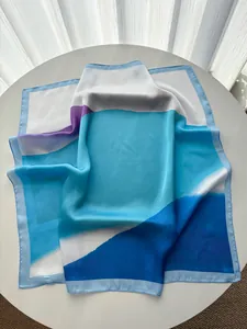 Detail of silk-like square scarf featuring blue geometric color blocks and fine stitching