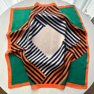 Détail d'un foulard en soie à rayures géométriques avec bordures orange et blocs verts