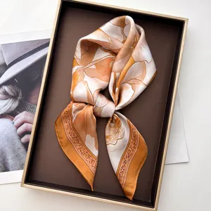 Dettaglio di sciarpa in seta a fiori arancio e beige piegata in confezione regalo