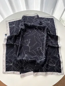Detailed view of black silk scarf with white floral print and gray satin edge detail