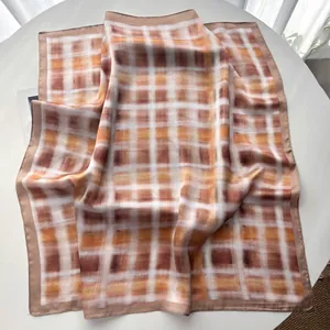 Detail van een zijdeachtige vierkante sjaal met oranje en bruin ruitpatroon en rolzoom