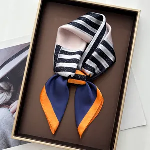 Foulard en soie à rayures bleu marine et orange, posé élégamment sur un plateau doré