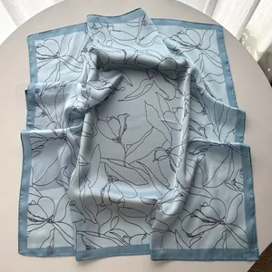 Detail of light blue silk square scarf with elegant black floral prints on a table