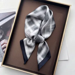 Detailopname van een grijs-wit geblokte zijden sjaal met zwarte rand in een geschenkdoos