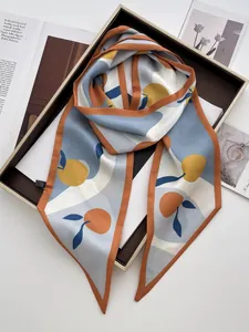 Detailed view of a fruit print satin scarf folded on a wooden tray with a lifestyle background